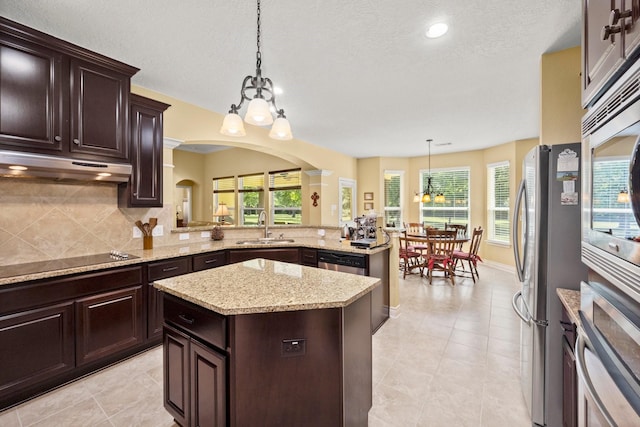 kitchen featuring a sink, stainless steel appliances, arched walkways, a center island, and a notable chandelier