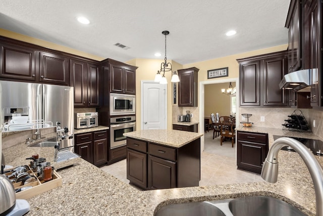 kitchen with a sink, under cabinet range hood, an inviting chandelier, dark brown cabinets, and appliances with stainless steel finishes