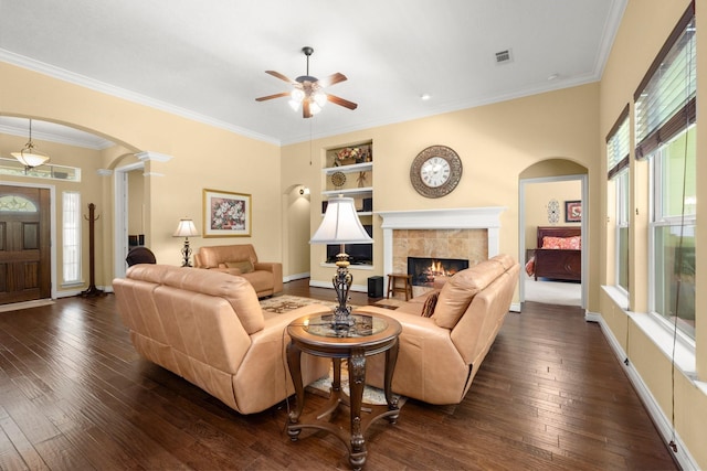living room featuring arched walkways, a ceiling fan, a tiled fireplace, and dark wood-type flooring