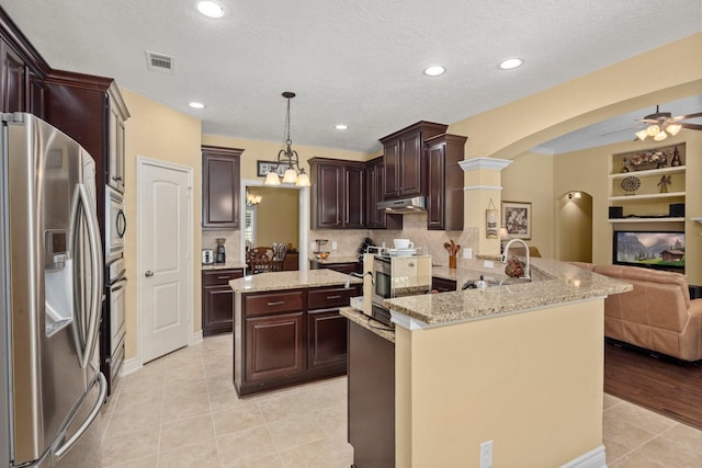 kitchen featuring a peninsula, under cabinet range hood, open floor plan, arched walkways, and appliances with stainless steel finishes
