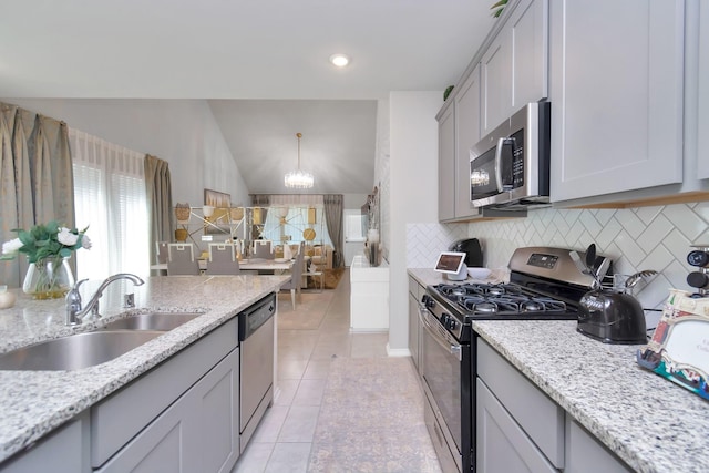 kitchen featuring a sink, decorative backsplash, light tile patterned flooring, a chandelier, and appliances with stainless steel finishes