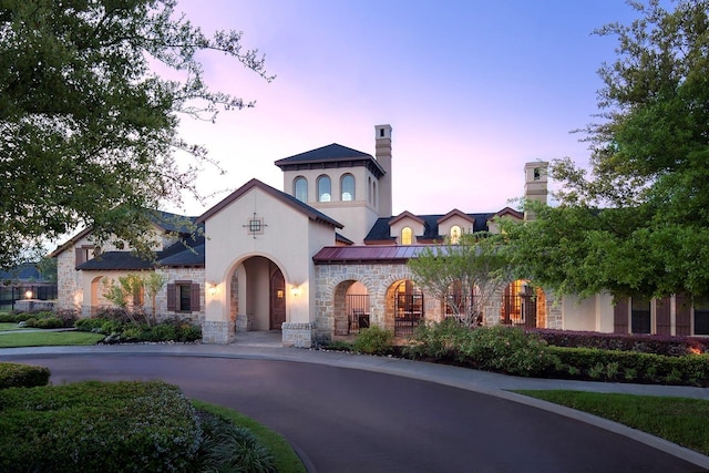 mediterranean / spanish home with stucco siding, a standing seam roof, stone siding, and metal roof