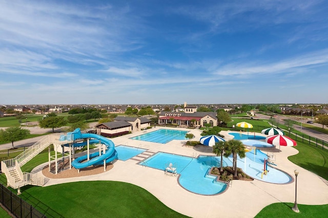 community pool with a water slide, fence, a water play area, and a patio