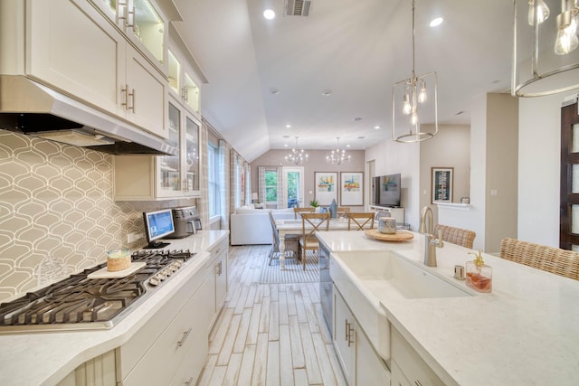 kitchen featuring lofted ceiling, a sink, visible vents, under cabinet range hood, and backsplash