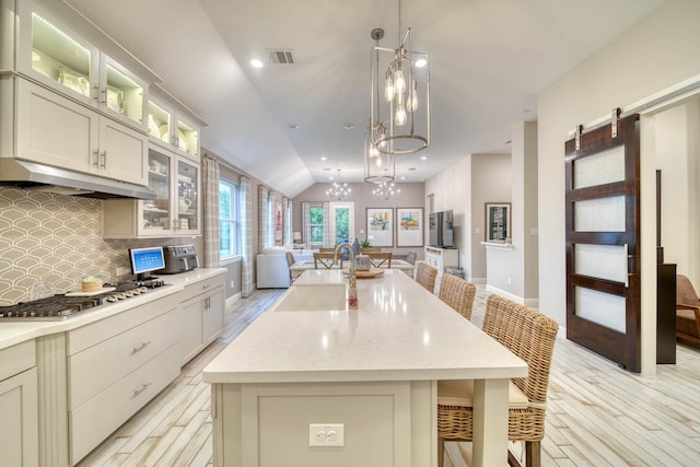 kitchen with stainless steel gas stovetop, under cabinet range hood, a sink, visible vents, and open floor plan