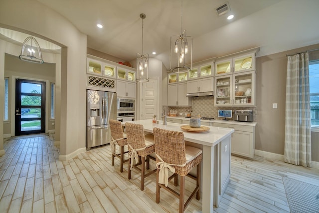 kitchen featuring an island with sink, appliances with stainless steel finishes, backsplash, light wood finished floors, and visible vents