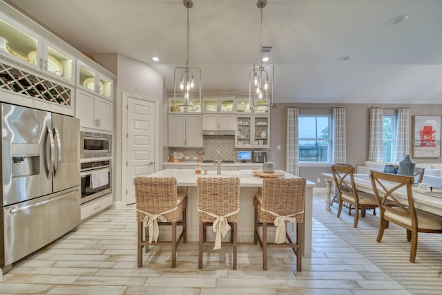 kitchen with decorative backsplash, decorative light fixtures, light countertops, appliances with stainless steel finishes, and an island with sink