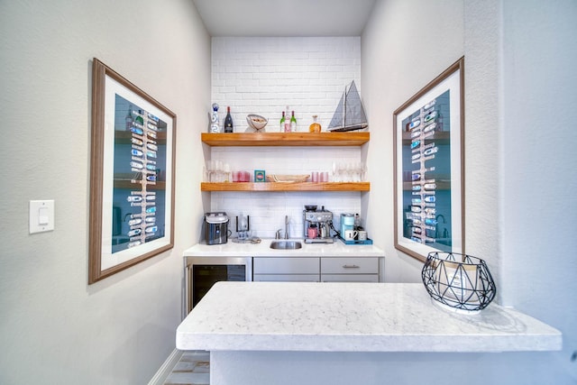 bar featuring decorative backsplash, a sink, beverage cooler, baseboards, and wet bar