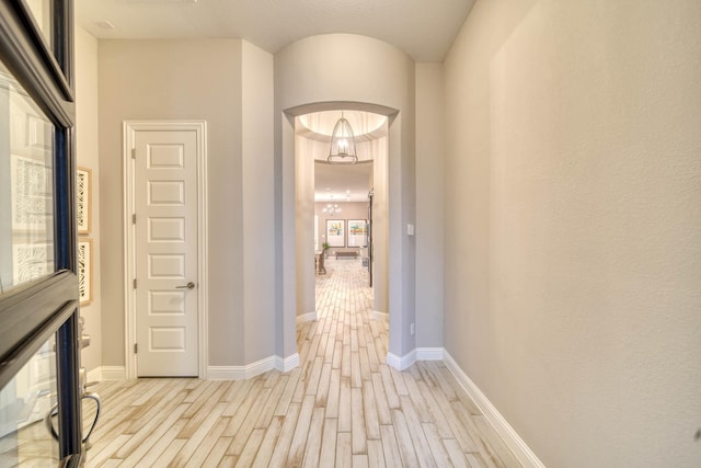hall featuring baseboards, light wood-type flooring, and arched walkways