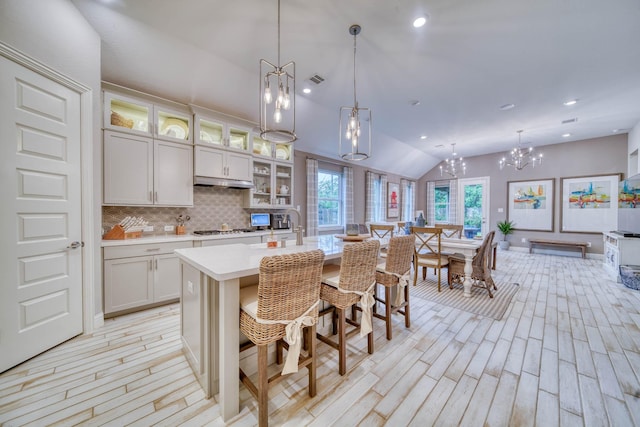 kitchen with stainless steel gas stovetop, light wood-style flooring, backsplash, light countertops, and lofted ceiling