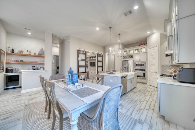 dining room featuring light wood finished floors, recessed lighting, visible vents, and beverage cooler