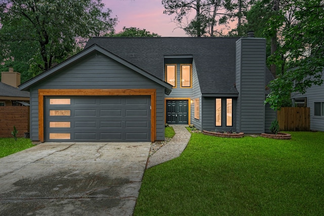 modern home with concrete driveway, a lawn, fence, and a shingled roof