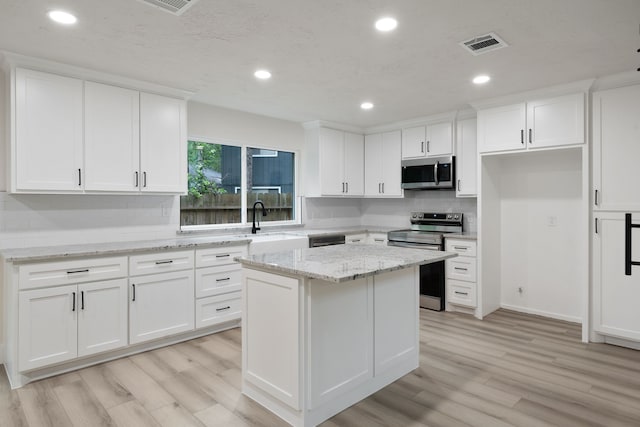 kitchen with light wood-style flooring, stainless steel appliances, white cabinetry, decorative backsplash, and visible vents