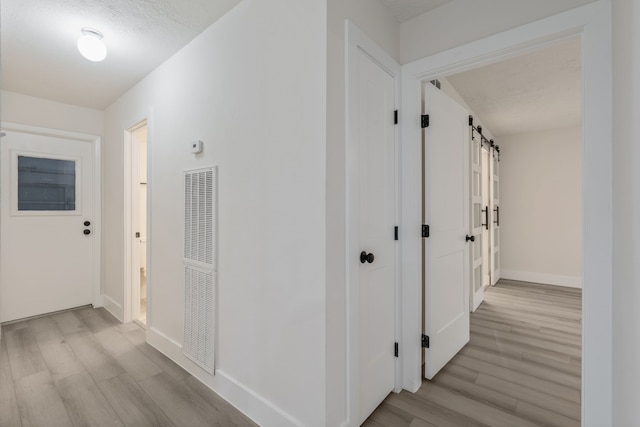hall featuring a barn door, baseboards, light wood-style flooring, and a heating unit