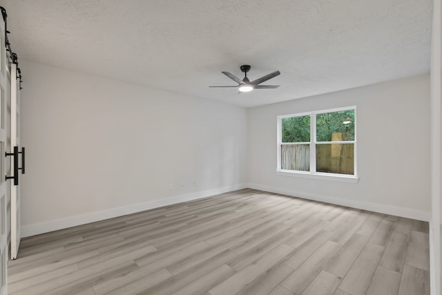 spare room featuring a textured ceiling, a barn door, ceiling fan, and light wood-type flooring