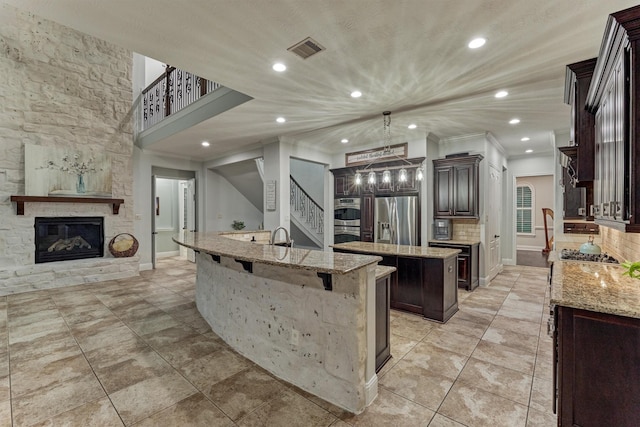 21603 Fairhaven Creek Dr, Cypress, TX 77433 - kitchen featuring appliances with stainless steel finishes, a spacious island, a fireplace, light stone counters, and recessed lighting