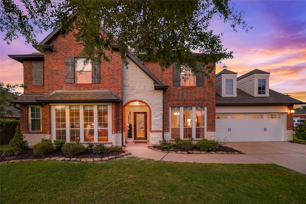 traditional home with a front lawn, driveway, stone siding, a garage, and brick siding