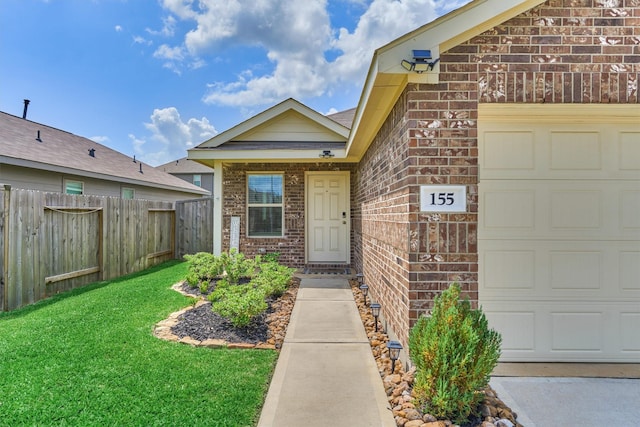 doorway to property featuring brick siding, an attached garage, a lawn, and fence