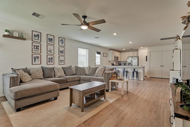 living room with light wood-type flooring, a ceiling fan, visible vents, and recessed lighting