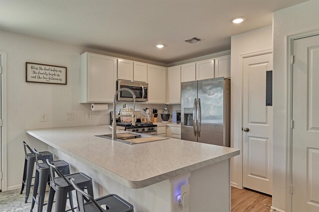 kitchen with stainless steel appliances, a peninsula, a kitchen bar, white cabinetry, and light countertops