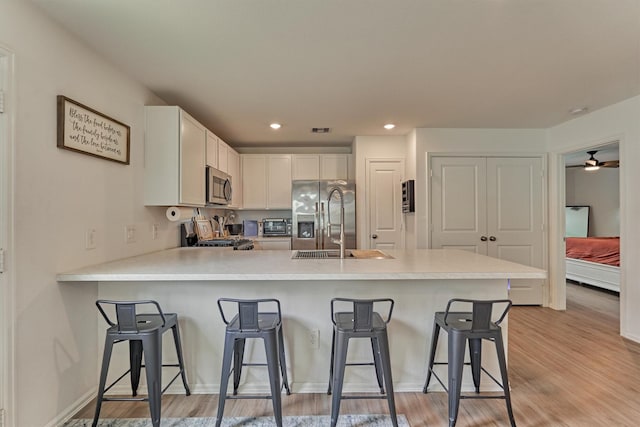 kitchen with light countertops, a peninsula, a kitchen bar, light wood-style flooring, and appliances with stainless steel finishes