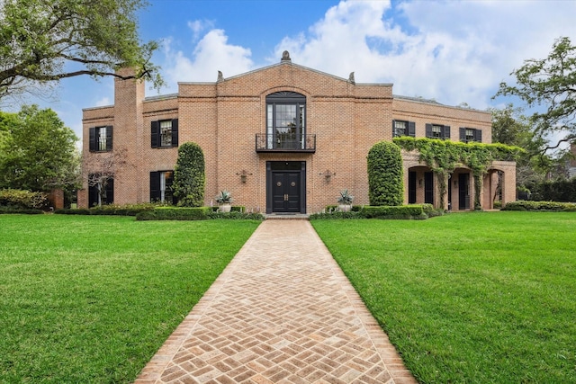 view of front of property featuring a front yard, a balcony, and brick siding