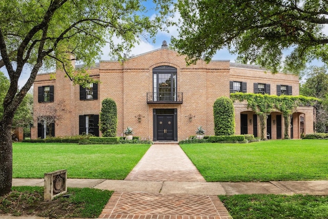 view of front of property featuring a front yard, a balcony, and brick siding