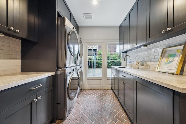washroom featuring a sink, cabinet space, visible vents, stacked washer and dryer, and brick floor