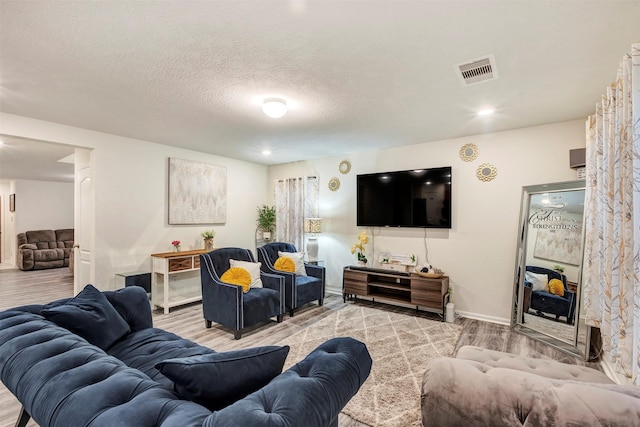 living room with a textured ceiling, baseboards, visible vents, and wood finished floors