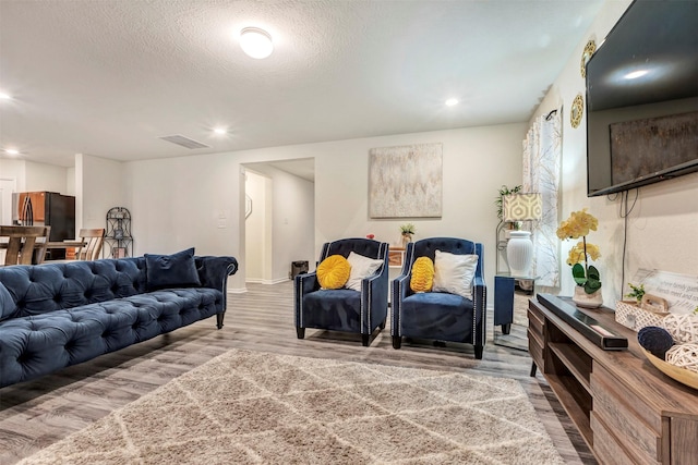 living area with a textured ceiling, recessed lighting, wood finished floors, and visible vents