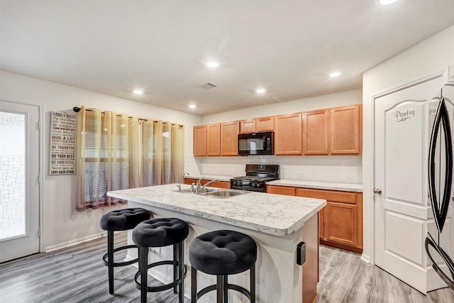 kitchen with visible vents, a sink, light countertops, black appliances, and light wood-style flooring
