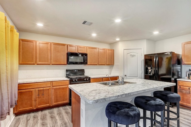 kitchen with visible vents, a breakfast bar, a sink, light wood finished floors, and black appliances