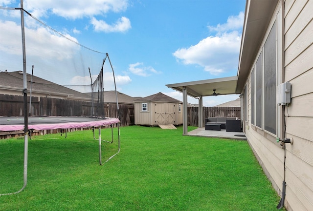 view of yard featuring a trampoline, an outdoor hangout area, a storage shed, ceiling fan, and a fenced backyard