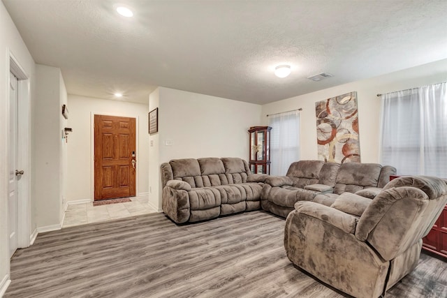 living room featuring baseboards, a textured ceiling, visible vents, and wood finished floors