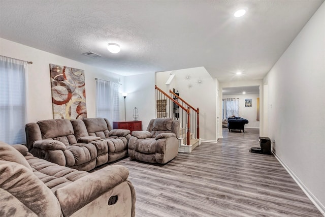 living room with light wood finished floors, a textured ceiling, baseboards, visible vents, and stairway