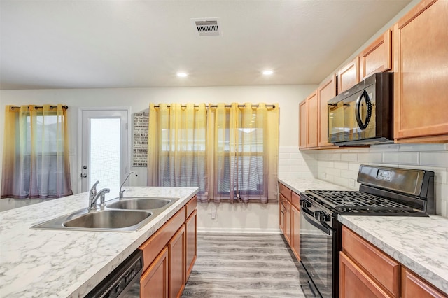 kitchen featuring visible vents, light wood-style floors, light countertops, a sink, and black appliances