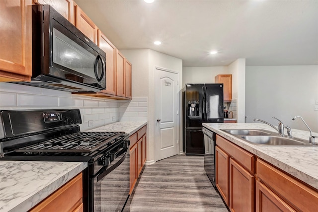 kitchen with a sink, wood finished floors, black appliances, backsplash, and light countertops