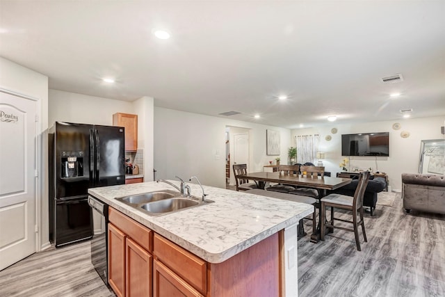 kitchen featuring a sink, black fridge with ice dispenser, dishwashing machine, open floor plan, and light wood-style floors