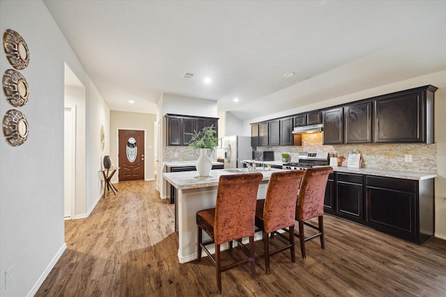 kitchen with dark wood-style floors, decorative backsplash, under cabinet range hood, and appliances with stainless steel finishes