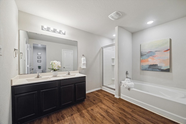 bathroom with a garden tub, wood finished floors, a sink, and double vanity