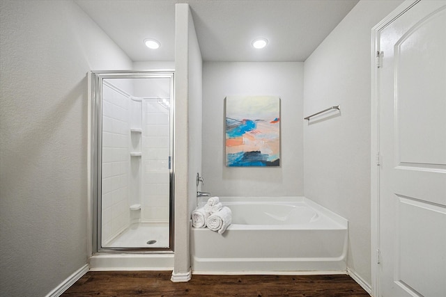 bathroom featuring a bath, baseboards, wood finished floors, and a shower stall