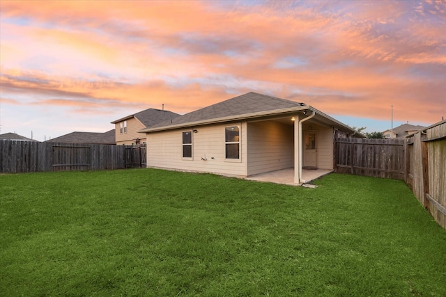 back of house at dusk featuring a patio area, a lawn, a fenced backyard, and roof with shingles