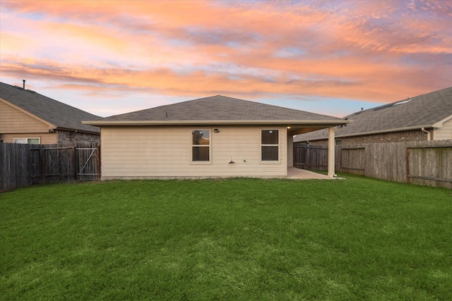 back of house at dusk with a fenced backyard, a yard, and a patio