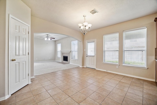 unfurnished living room featuring baseboards, visible vents, ceiling fan with notable chandelier, a tile fireplace, and light tile patterned floors