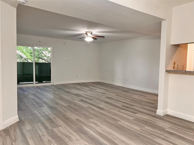 spare room with wood finished floors, a ceiling fan, and baseboards