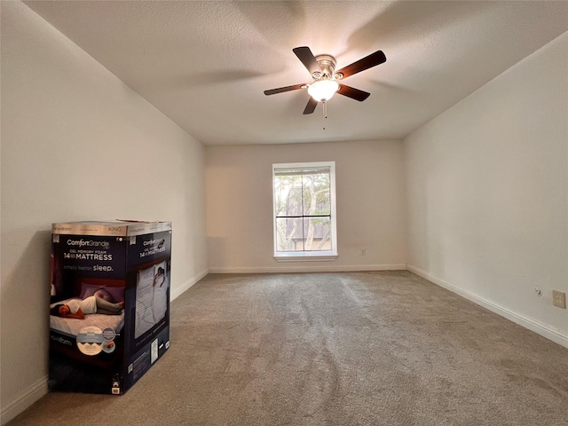 carpeted spare room with a ceiling fan and baseboards