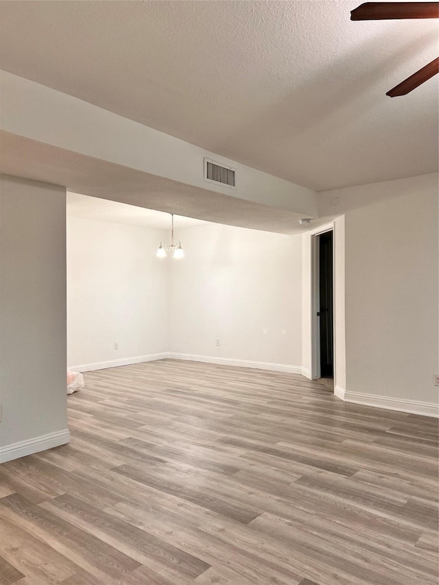 below grade area with light wood finished floors, visible vents, baseboards, a textured ceiling, and ceiling fan with notable chandelier