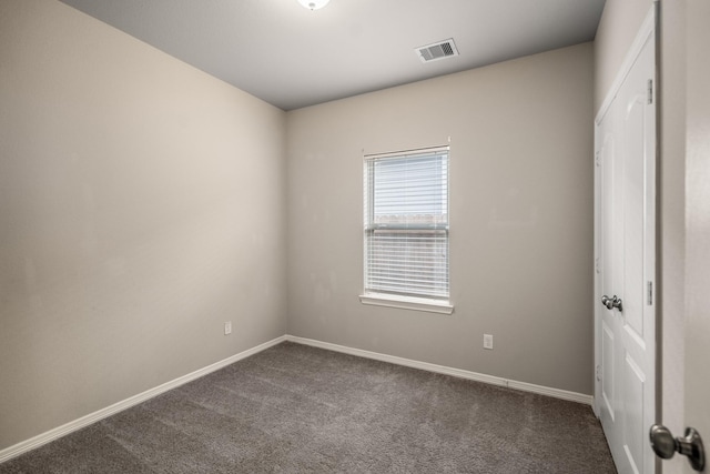spare room featuring baseboards, dark colored carpet, and visible vents