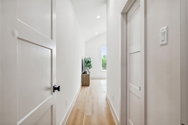 corridor with baseboards, vaulted ceiling, and light wood-type flooring