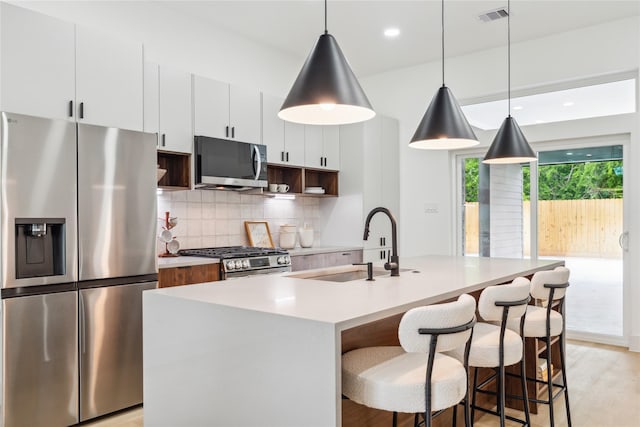 kitchen featuring stainless steel appliances, visible vents, a sink, a kitchen island with sink, and tasteful backsplash